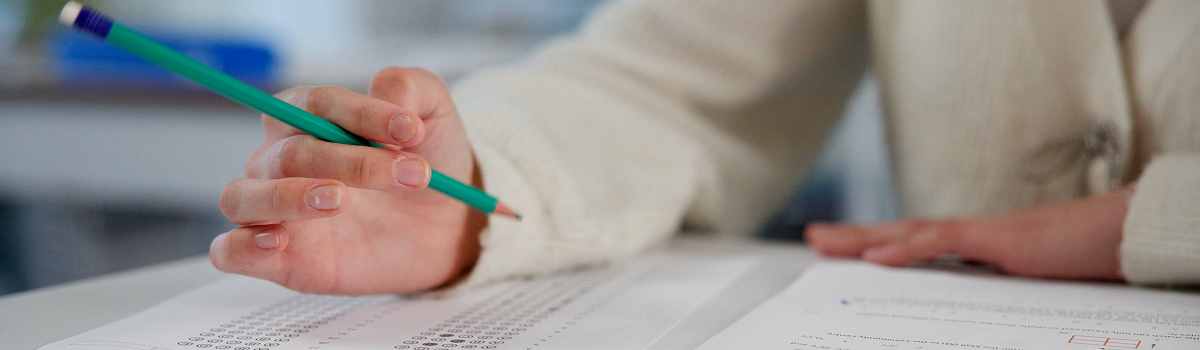 Eine Hand füllt einen Multiple-Choice-Test mit einem grünen Bleistift aus.